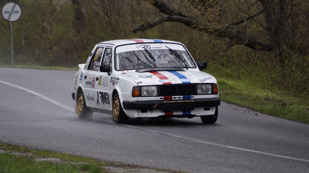 a white car driving down a road next to a forest