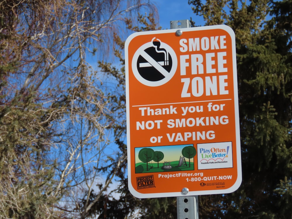 a no smoking sign on a pole in front of some trees