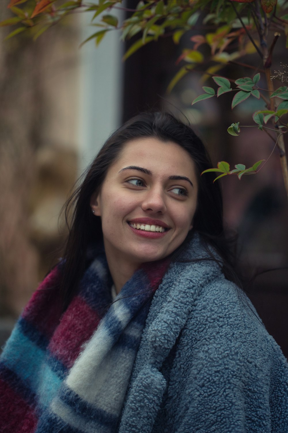 a smiling woman wrapped in a blanket next to a tree