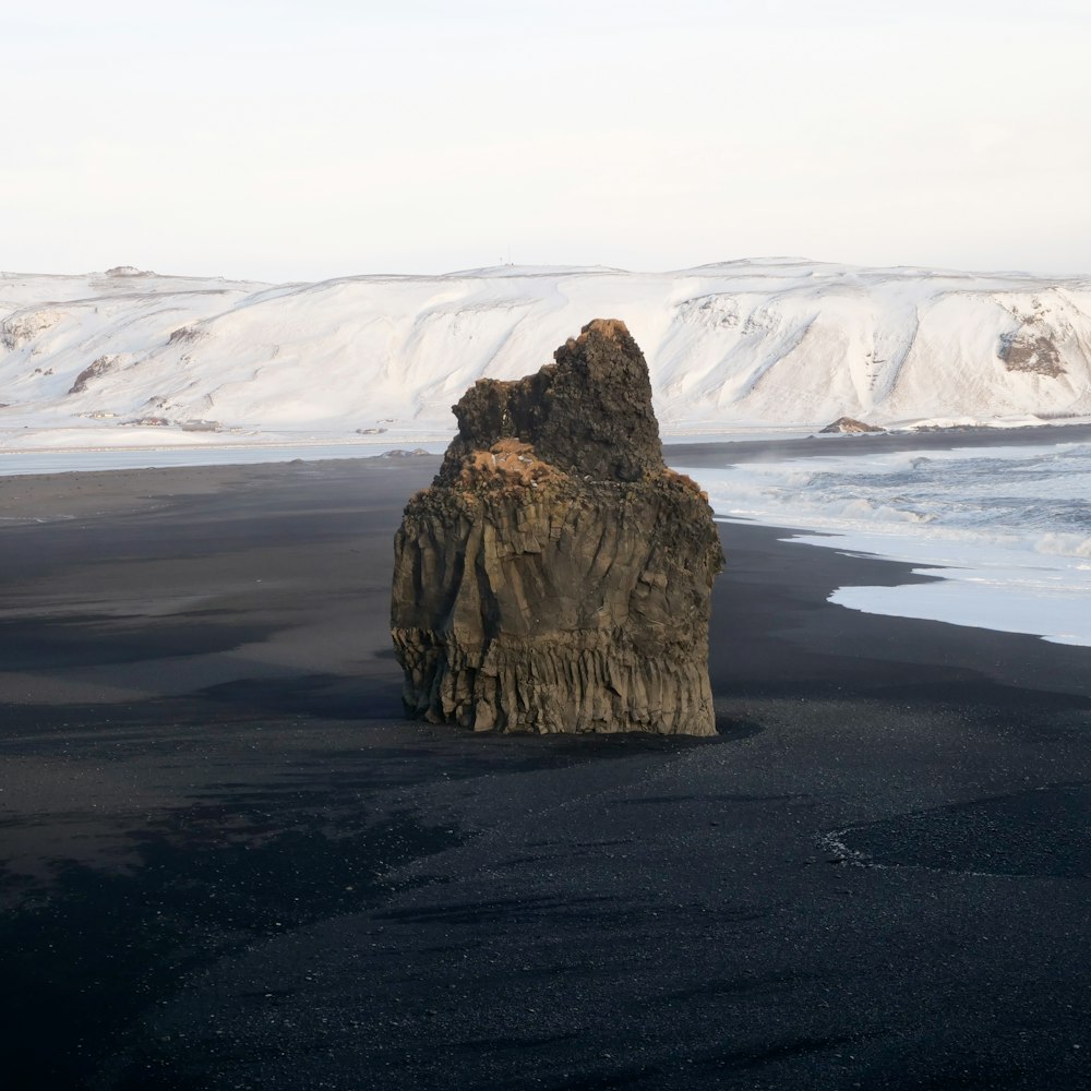 a large rock sitting on top of a black sand beach