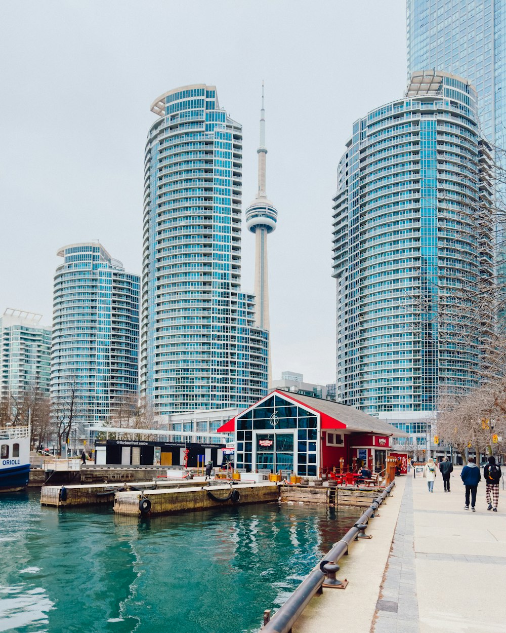 a group of people walking along a river next to tall buildings