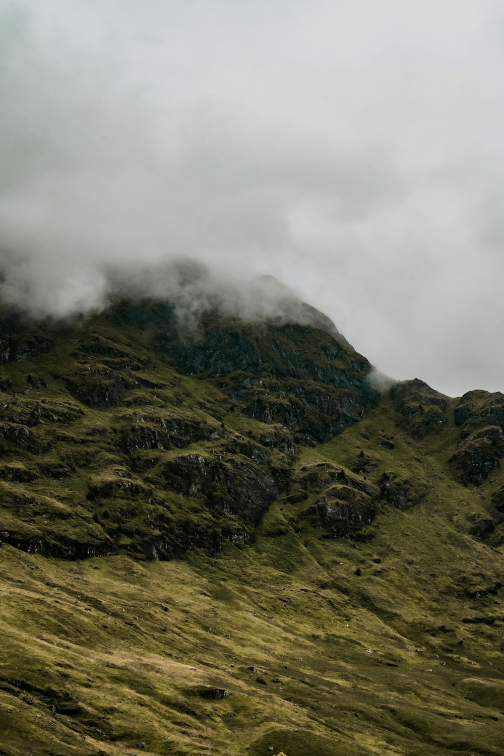 a mountain covered in green grass under a cloudy sky