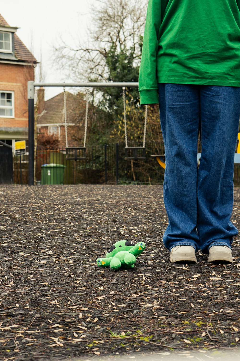 a person standing next to a green stuffed animal