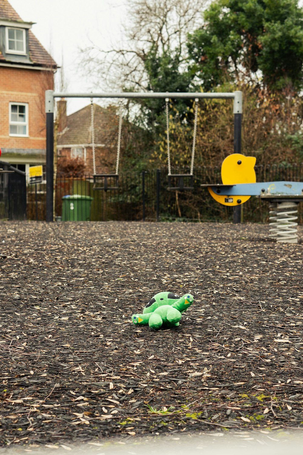 a green teddy bear laying on the ground in a park