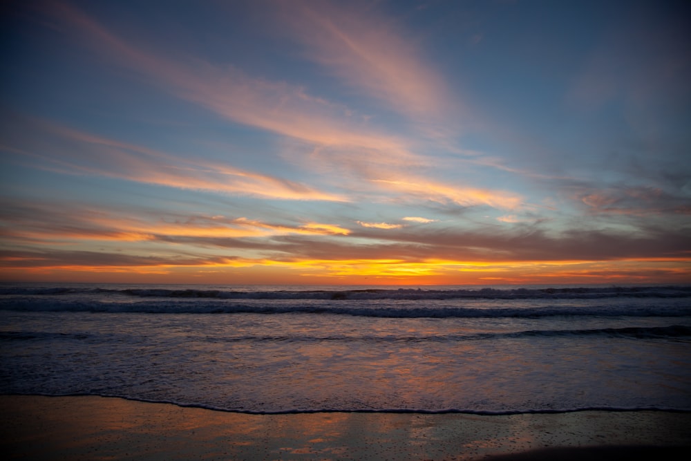 the sun is setting over the ocean on a cloudy day