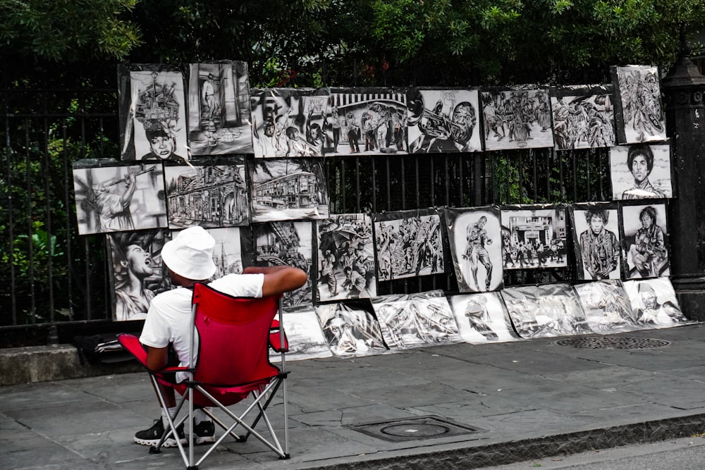 a man sitting in a red chair in front of a wall with pictures on it