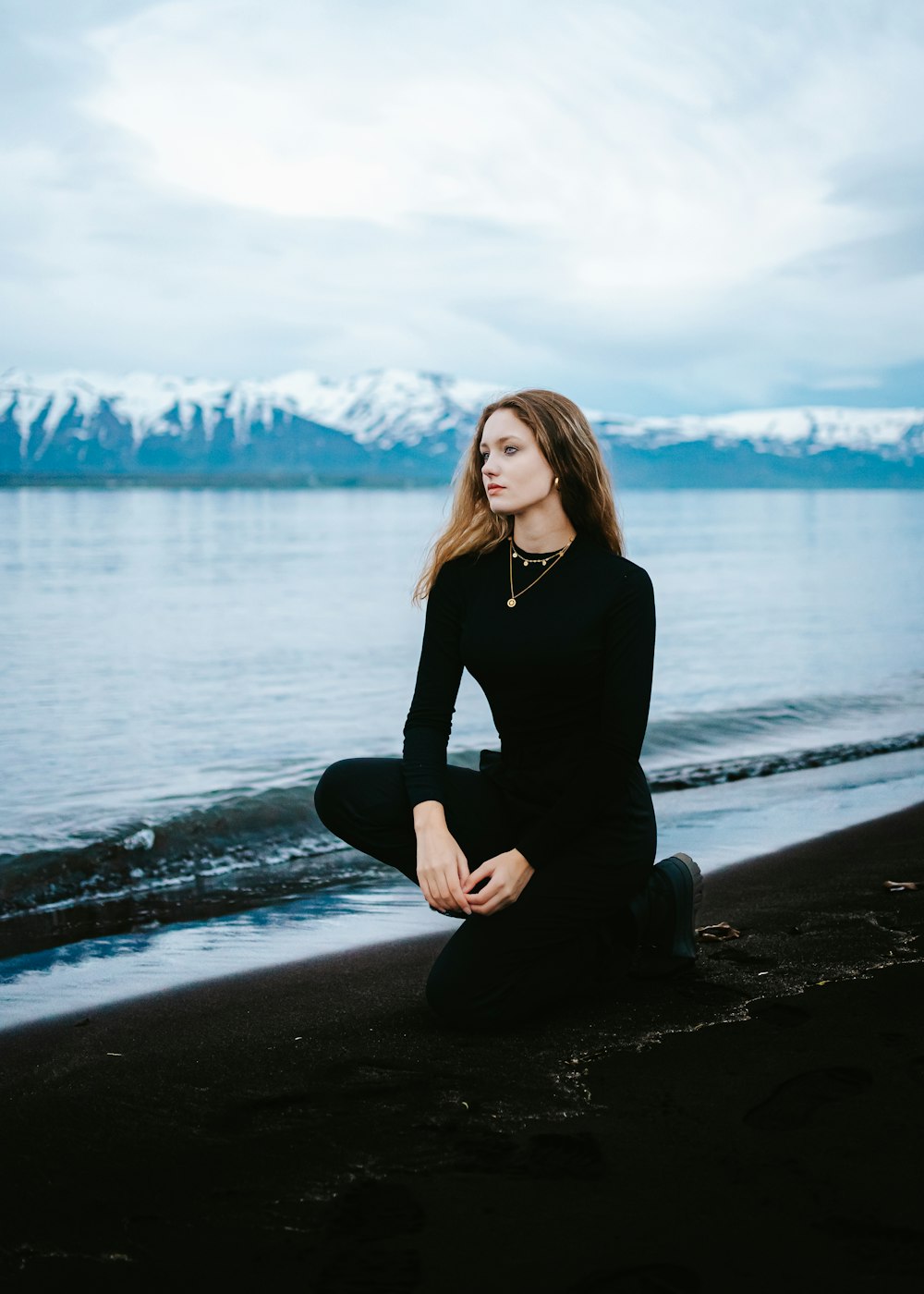 a woman is sitting on the beach by the water