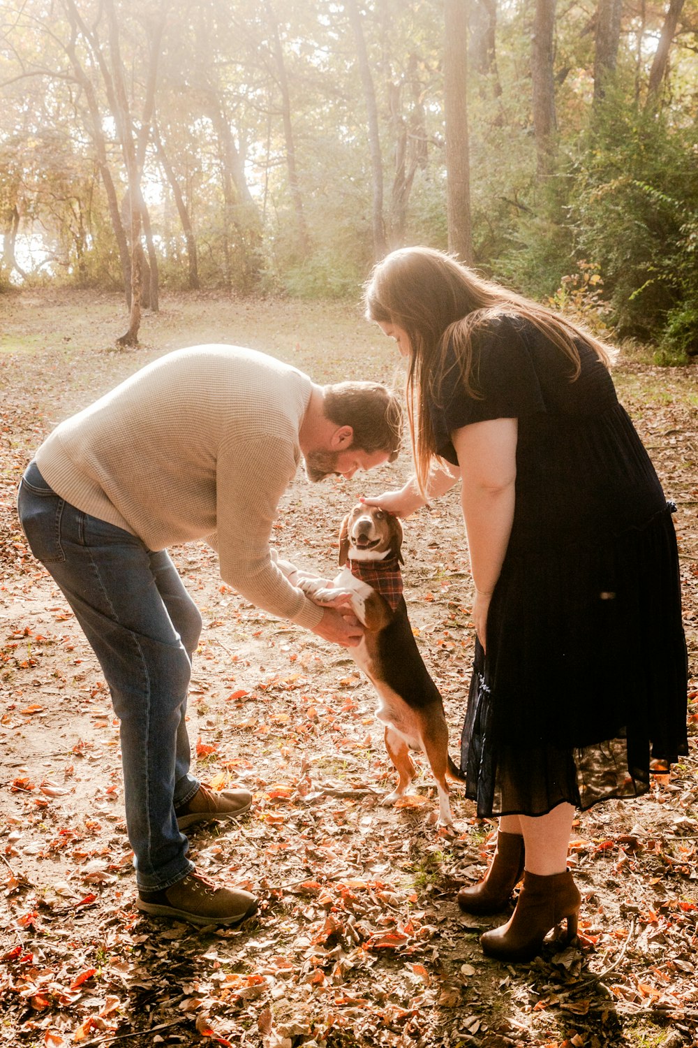 a man and woman petting a dog in the woods