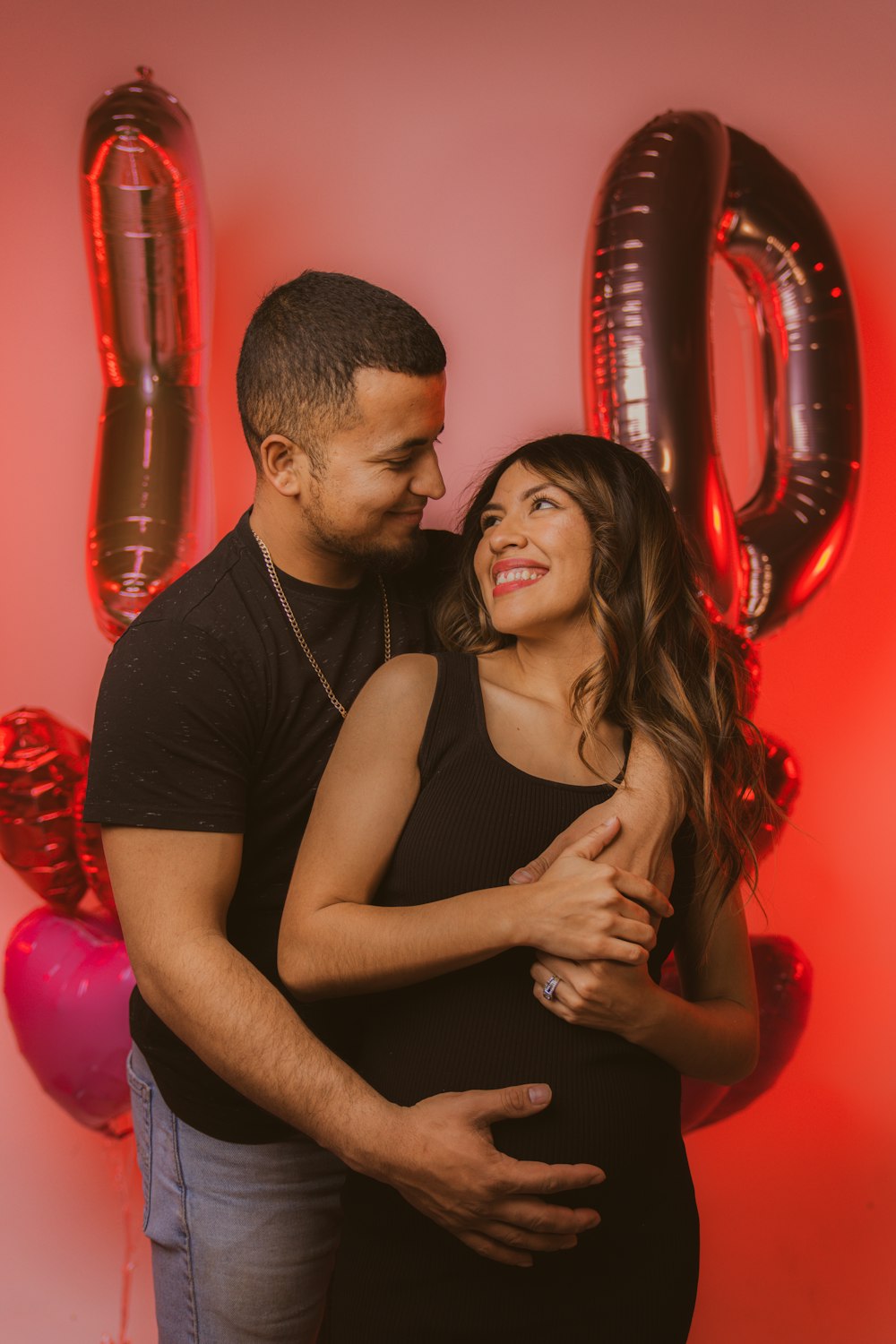 a pregnant couple embracing in front of balloons