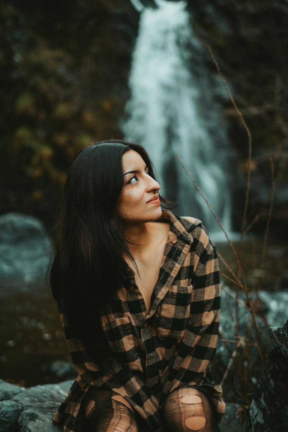 a woman sitting on a rock in front of a waterfall