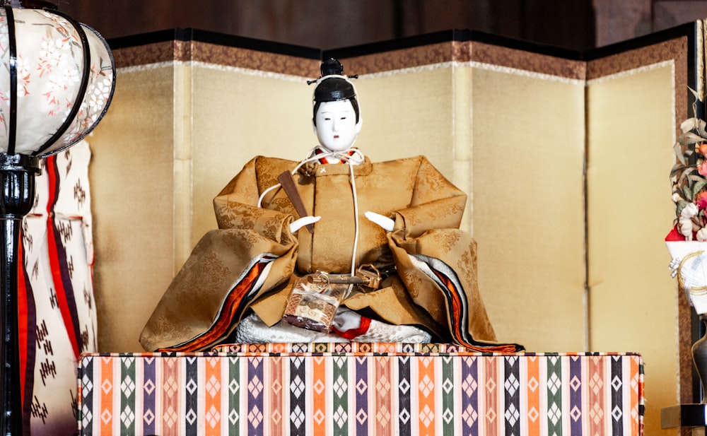 Una muñeca geisha sentada en una mesa junto a una lámpara