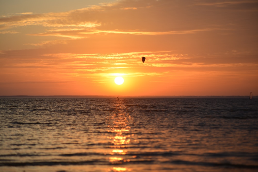 the sun is setting over the ocean with a kite flying in the sky