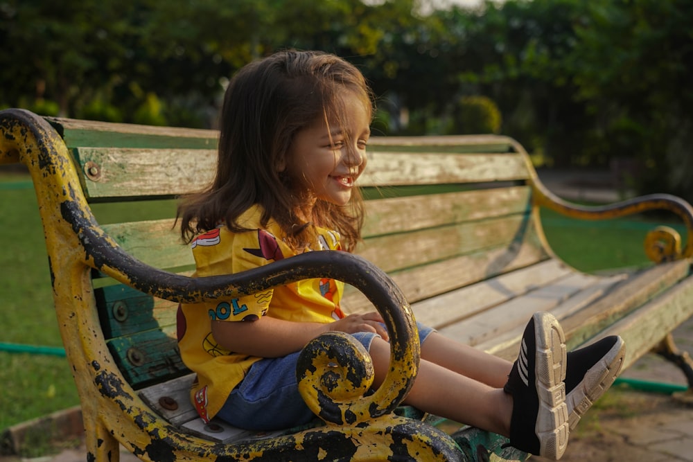 a little girl sitting on top of a wooden bench