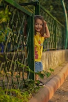 a little girl standing next to a green fence