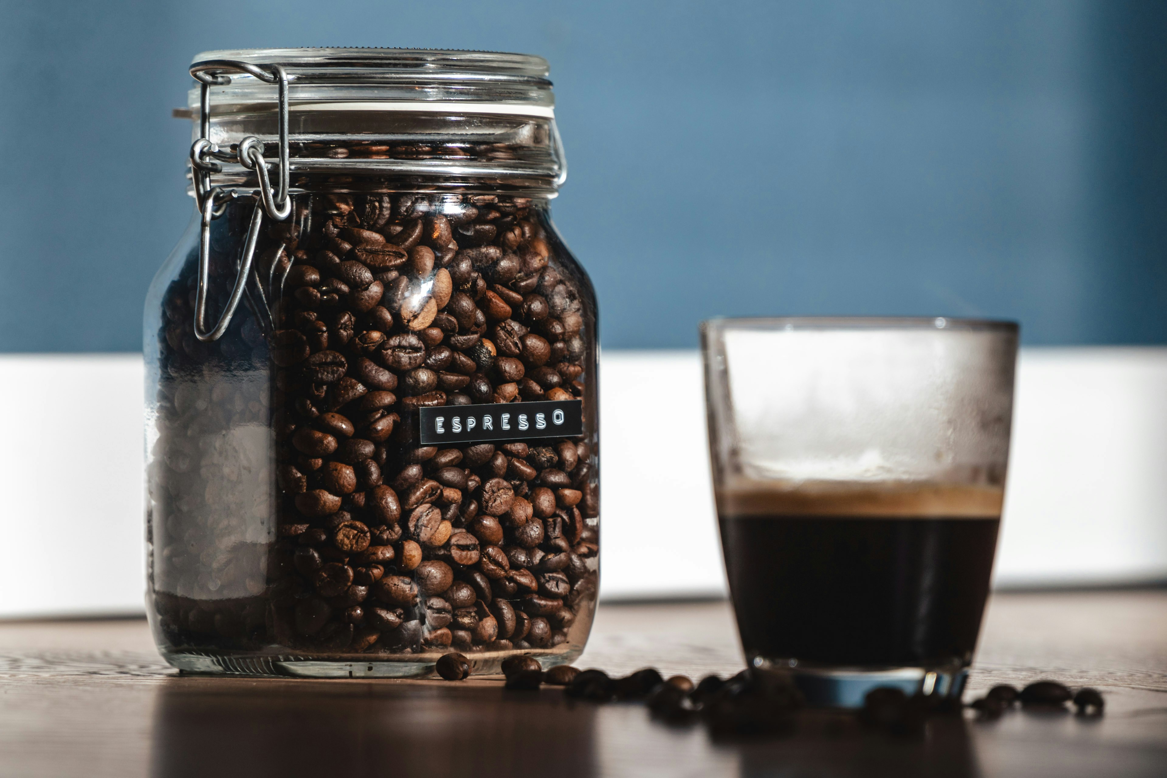 ein Glas Kaffee neben einem Glas Kaffeebohnen