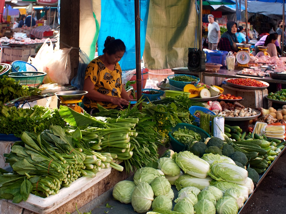 a woman sitting at a table filled with lots of vegetables