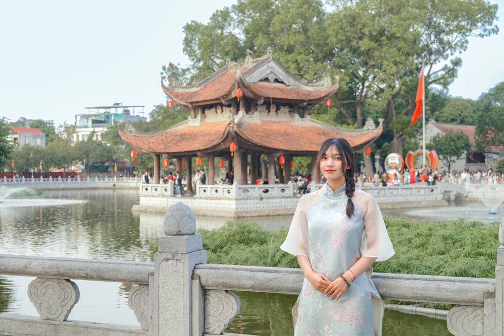 a woman standing in front of a pond with a pagoda in the background