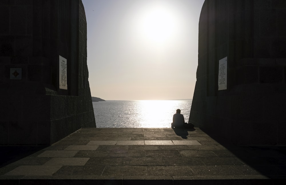 a person sitting on a stone walkway near the ocean