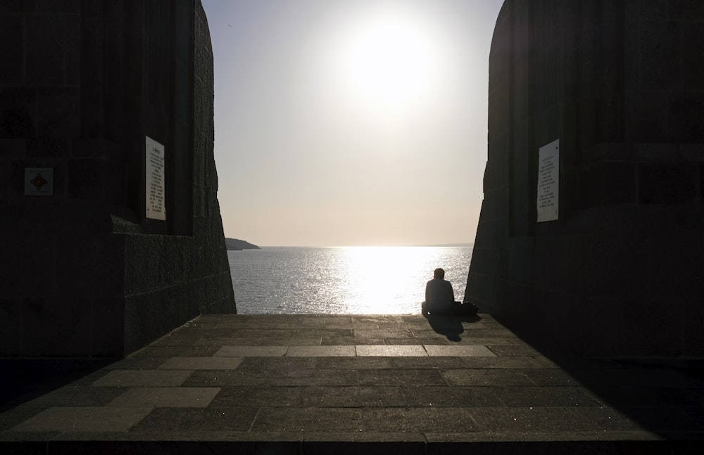 una persona sentada en una pasarela de piedra cerca del océano