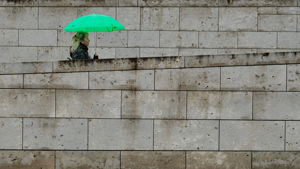 a person sitting on a ledge with a green umbrella