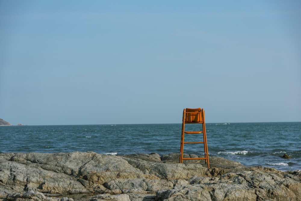 a wooden chair sitting on top of a rocky beach