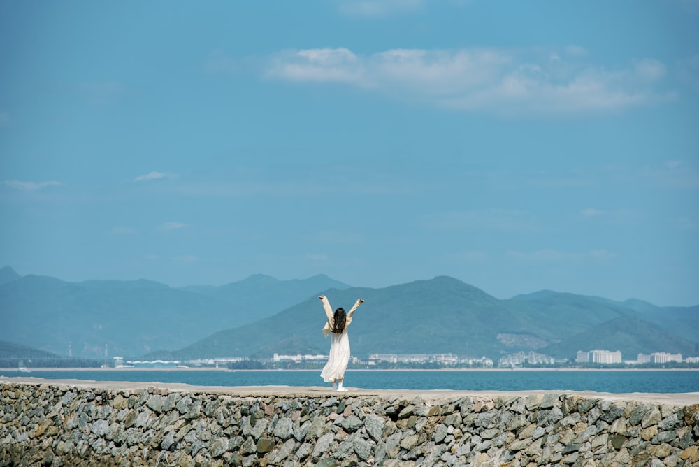 a woman standing on a rock wall with her arms in the air