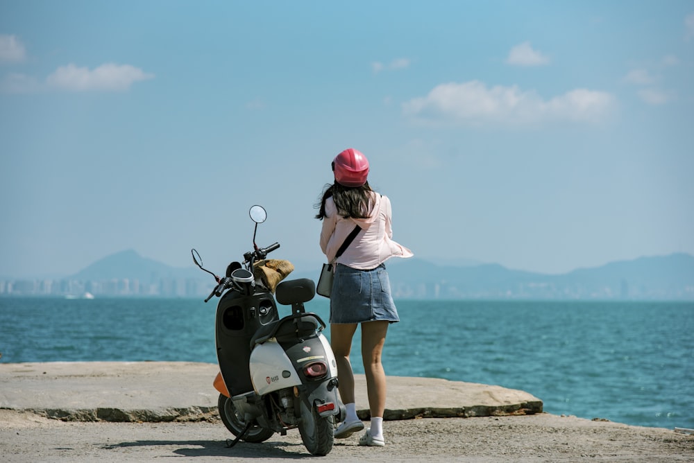 a woman standing next to a scooter near the ocean