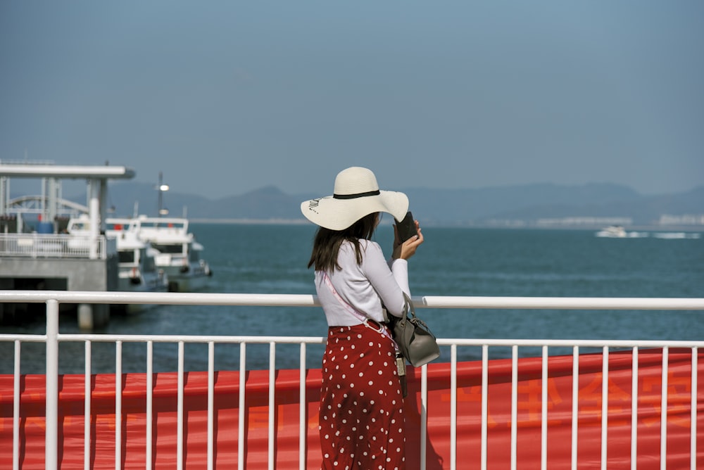 a woman wearing a white hat looking out over the water