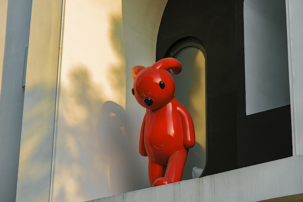 a red teddy bear sitting on top of a window sill