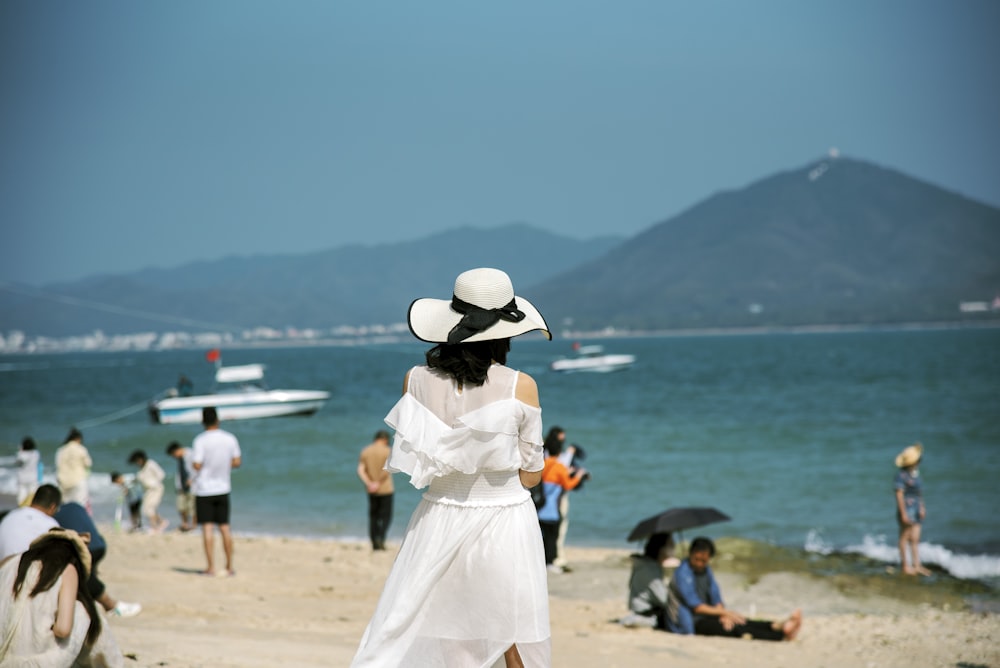 a woman in a white dress and hat standing on a beach