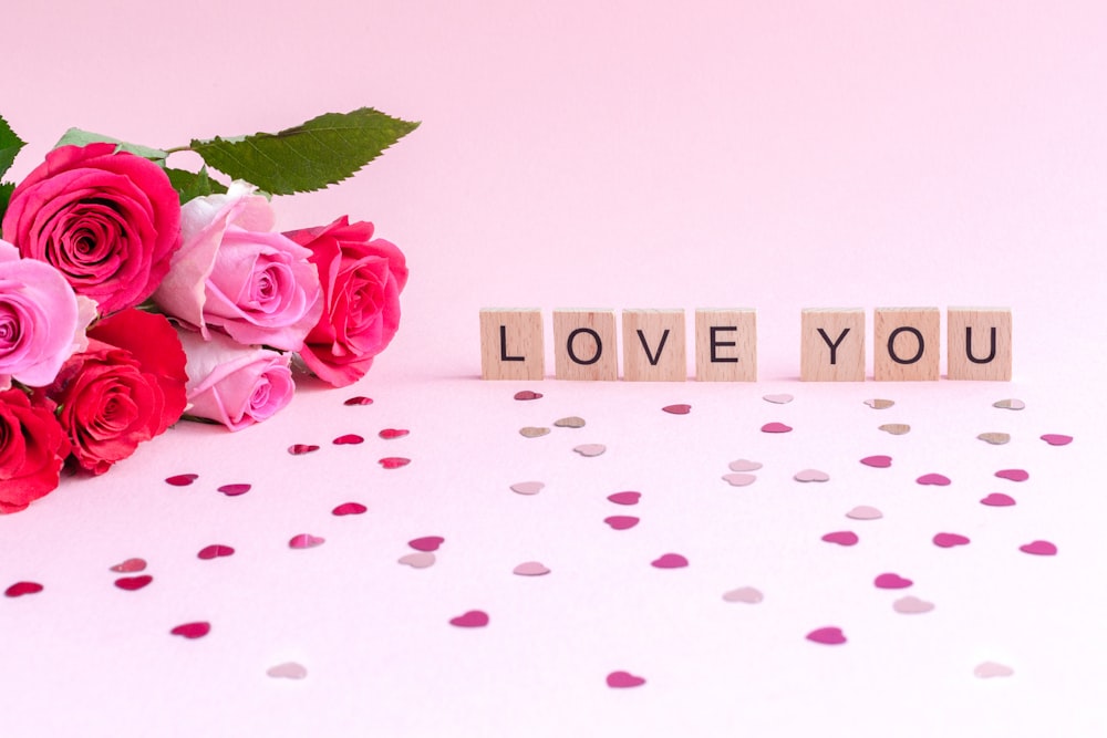 a bouquet of pink roses next to a block spelling love you
