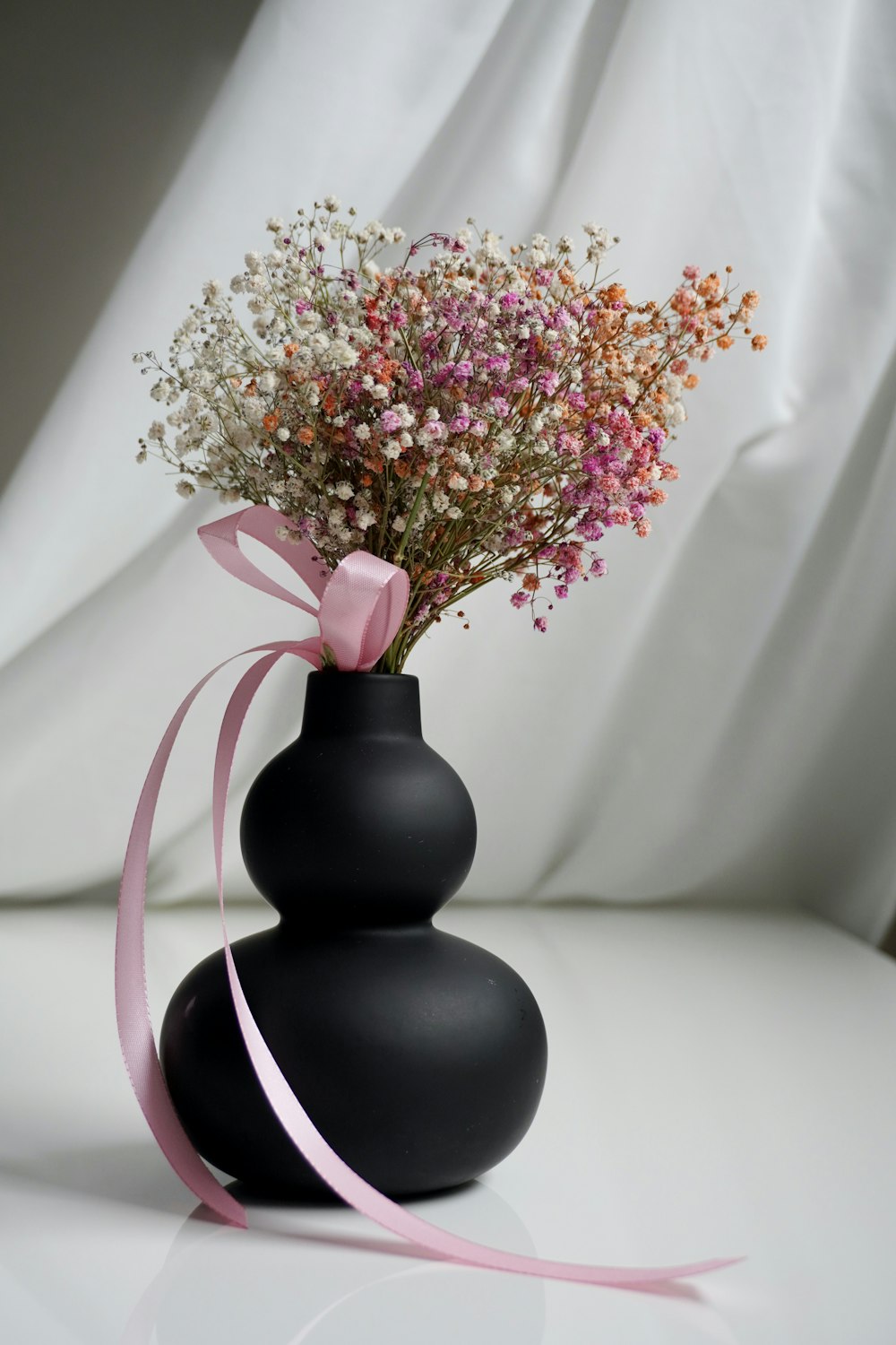 a black vase with a pink ribbon tied around it