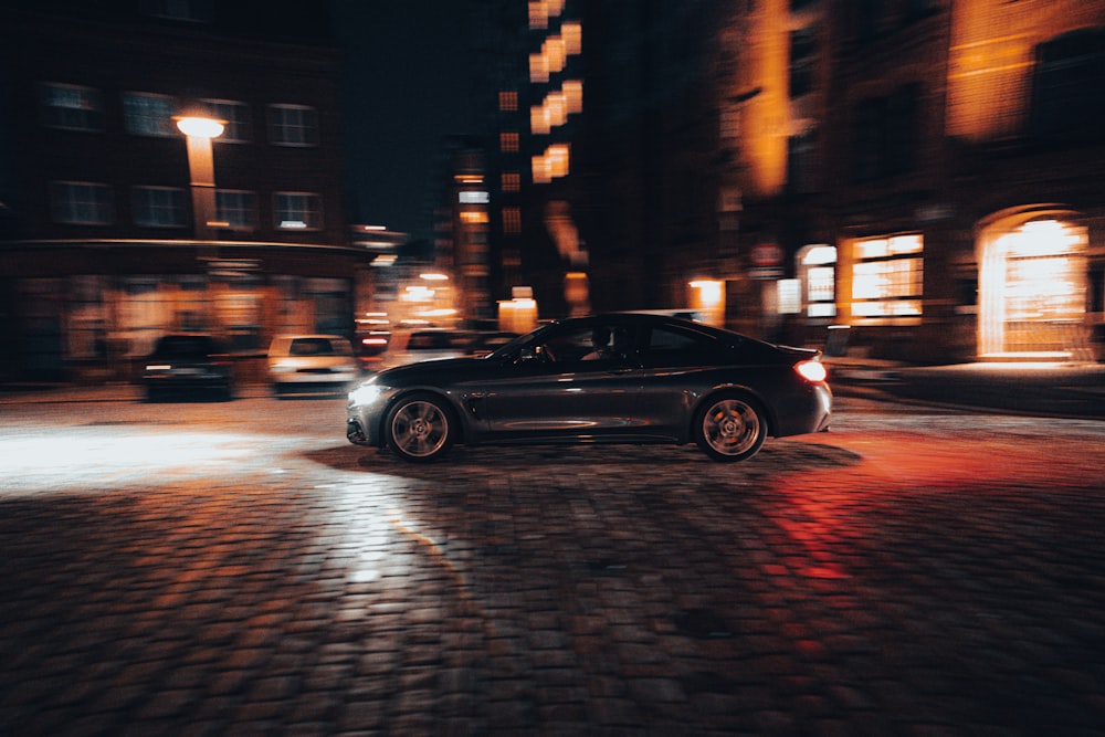 a black sports car parked on a cobblestone street at night