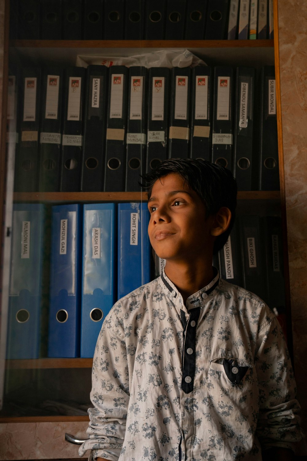 a young boy standing in front of a book shelf