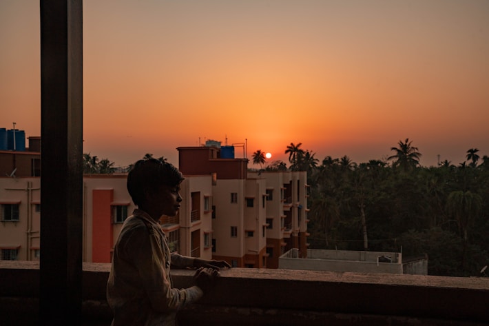 a boy standing on top of a balcony watching the sunset