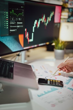 a mão de uma pessoa analisando métricas financeiras em frente a um monitor