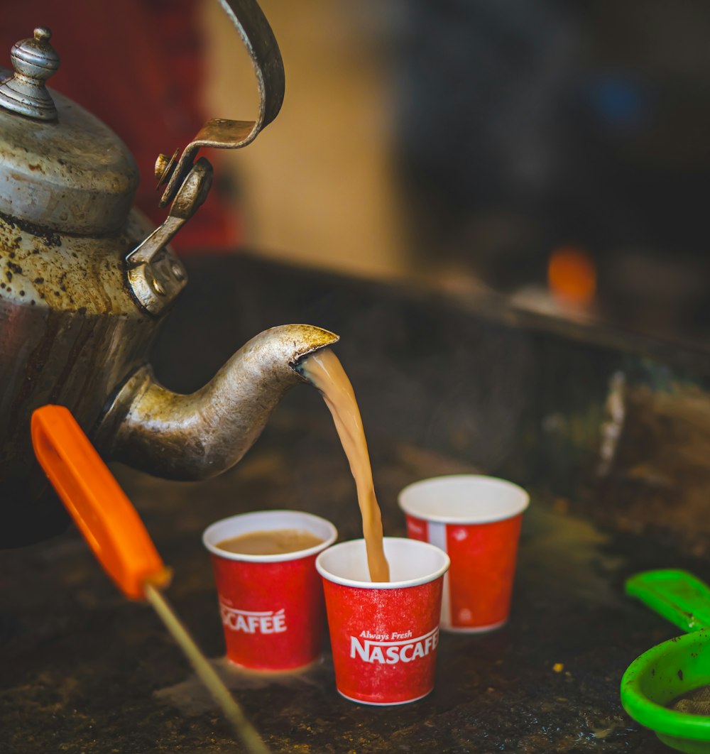 a tea kettle pouring tea into four cups