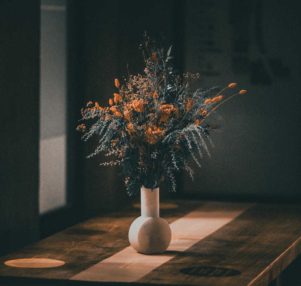 a white vase filled with lots of flowers on top of a wooden table