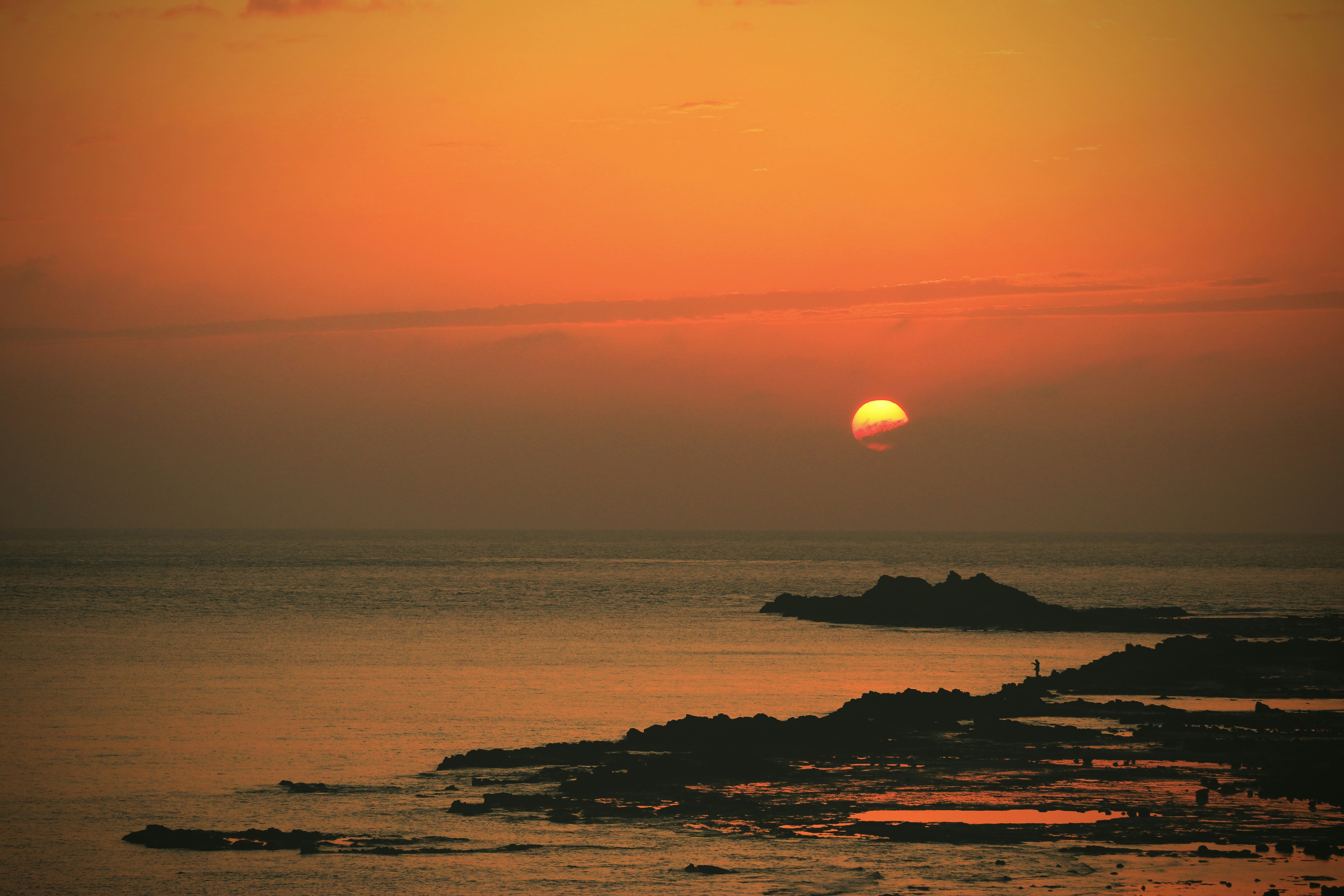 the sun is setting over the ocean with rocks in the foreground