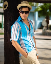 a man leaning against a tree wearing a hat and sunglasses