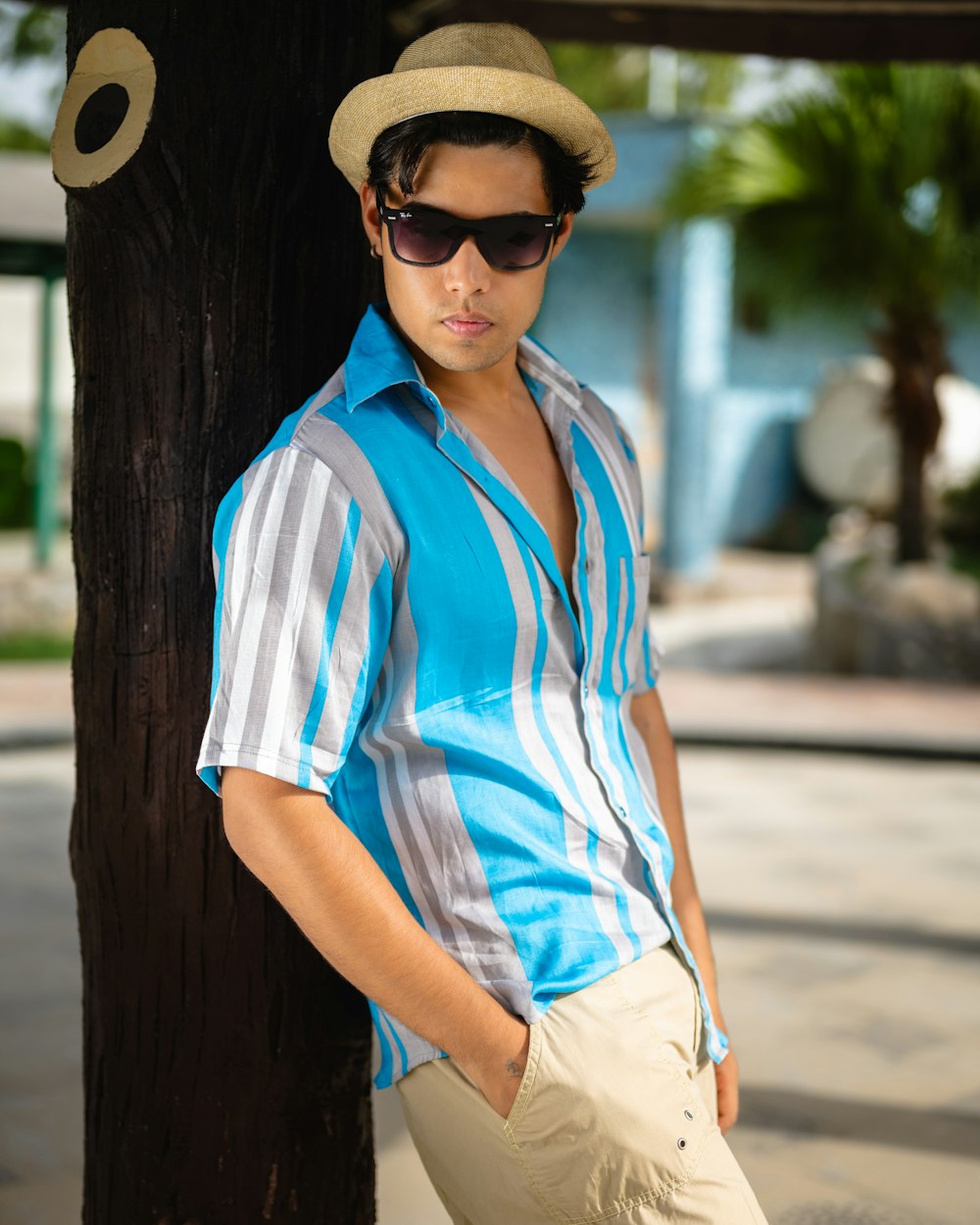 a man leaning against a tree wearing a hat and sunglasses