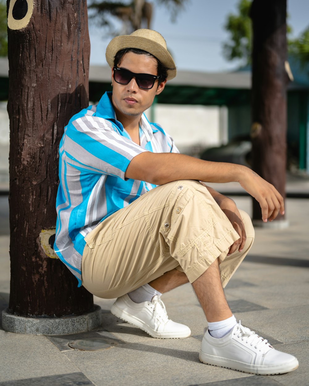 a man sitting against a tree wearing a hat and sunglasses