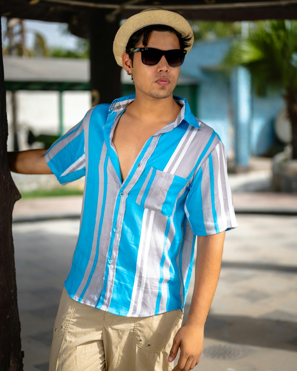 a man in a hat and sunglasses leaning against a tree