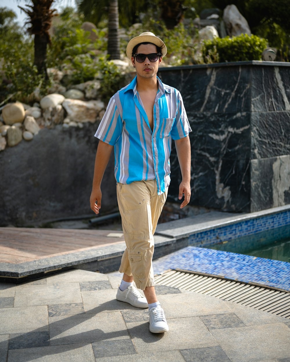 a man in a blue shirt and tan pants walking by a pool