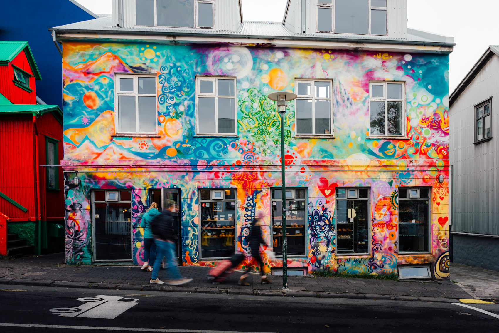 A brightly painted mural across a small Reykjavík building as people walk past
