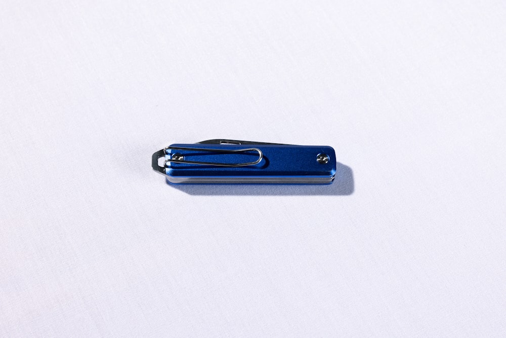 a blue clip with a black handle on a white surface