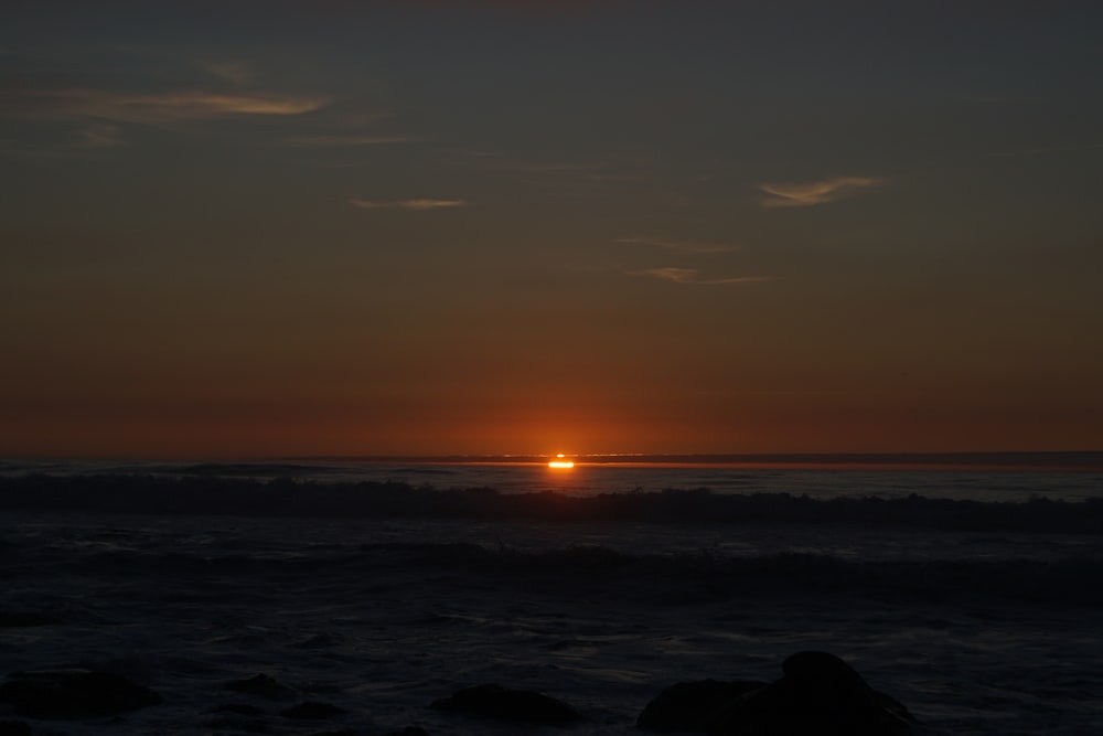 the sun is setting over the ocean on a cloudy day