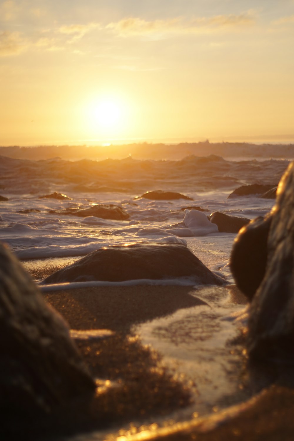 the sun is setting over the ocean with rocks in the foreground