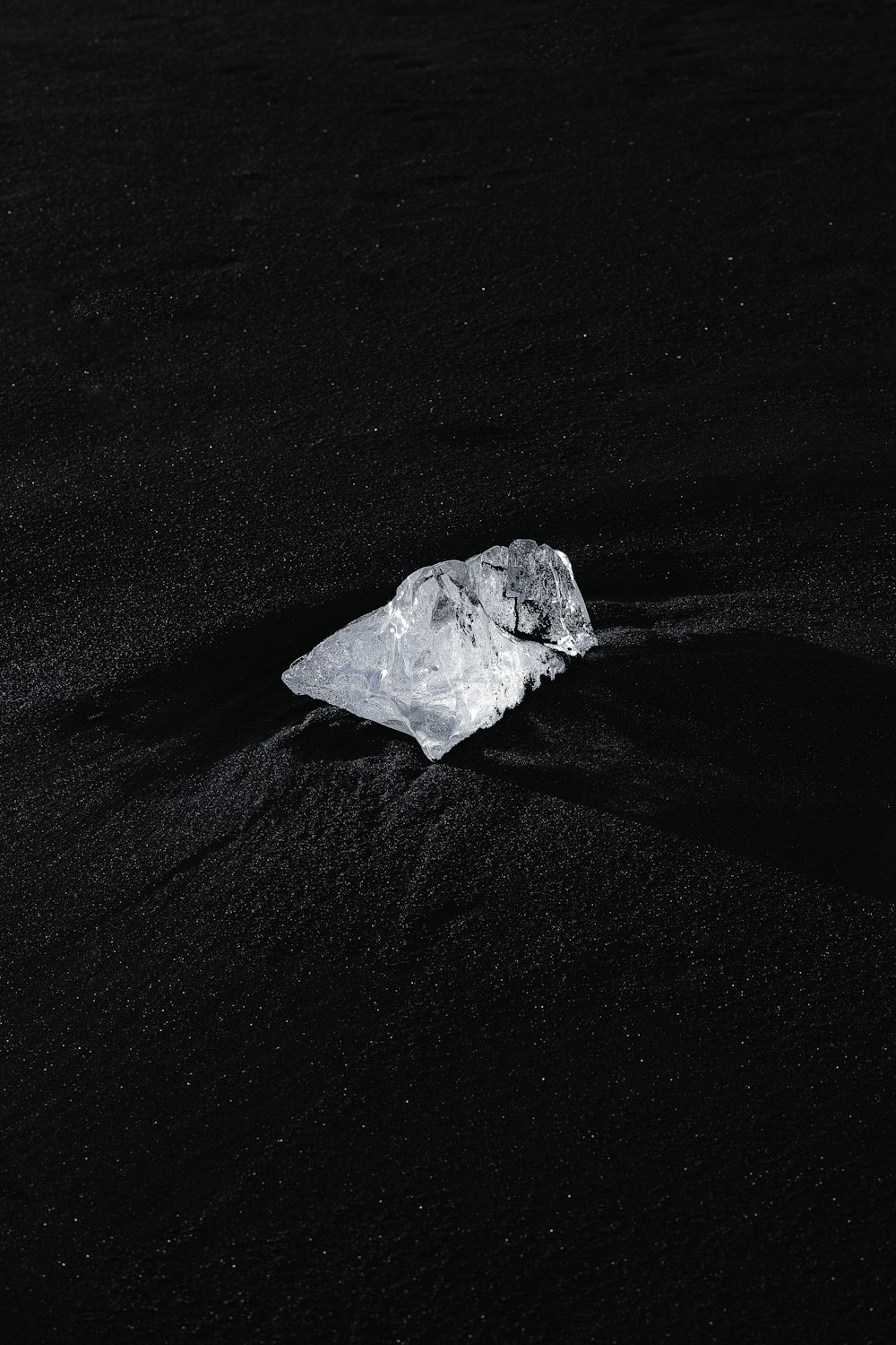 a piece of ice sitting on top of a black sand beach