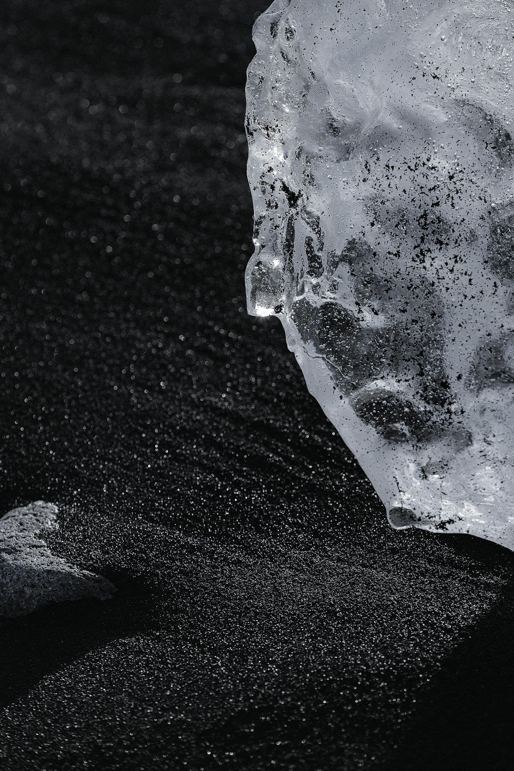 a piece of ice sitting on top of a black sand beach